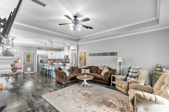 living area with dark wood-style flooring, visible vents, crown molding, ceiling fan, and a raised ceiling