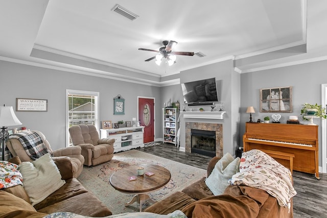 living room with a tray ceiling, ceiling fan, visible vents, a tile fireplace, and wood finished floors