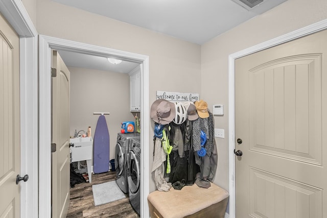 washroom with visible vents, wood finished floors, cabinet space, a sink, and washing machine and dryer