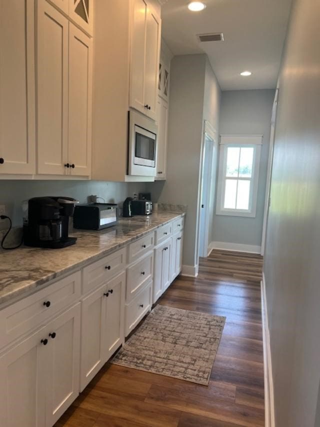 1015 Hardy Rd, Dothan, AL 36301 - kitchen featuring stainless steel microwave, white cabinetry, light stone countertops, dark wood-style floors, and glass insert cabinets