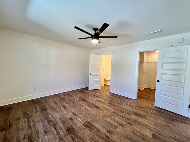 unfurnished bedroom featuring dark wood-type flooring, a walk in closet, ensuite bath, a closet, and ceiling fan