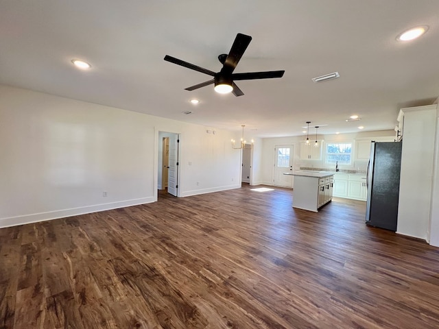 unfurnished living room featuring ceiling fan with notable chandelier and dark hardwood / wood-style floors