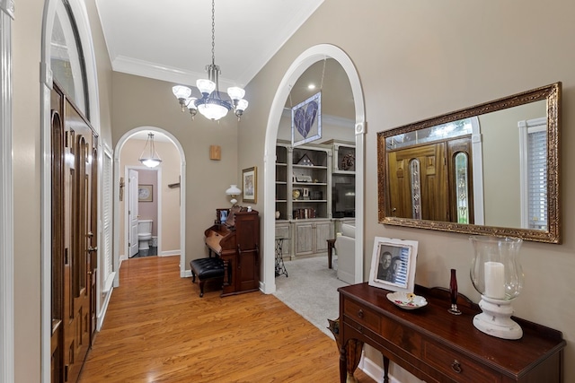 corridor featuring crown molding, light hardwood / wood-style flooring, and an inviting chandelier