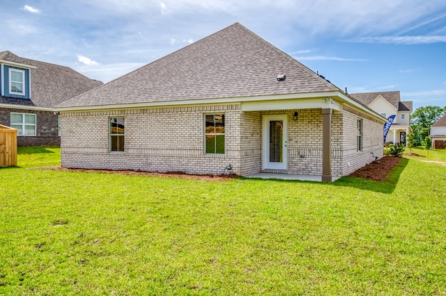 rear view of house with a lawn, brick siding, and roof with shingles