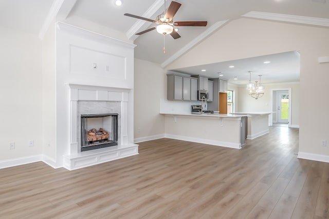 unfurnished living room featuring ceiling fan with notable chandelier, light wood-style floors, vaulted ceiling, ornamental molding, and a high end fireplace
