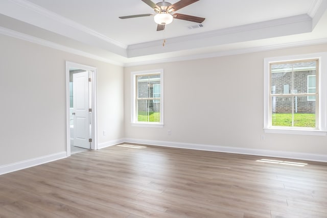 spare room with ornamental molding, light wood-type flooring, visible vents, ceiling fan, and a tray ceiling