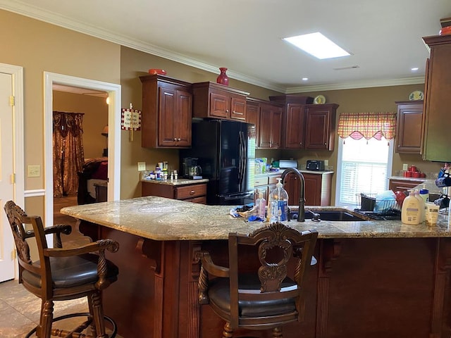 kitchen with black refrigerator, a breakfast bar, kitchen peninsula, crown molding, and light stone countertops