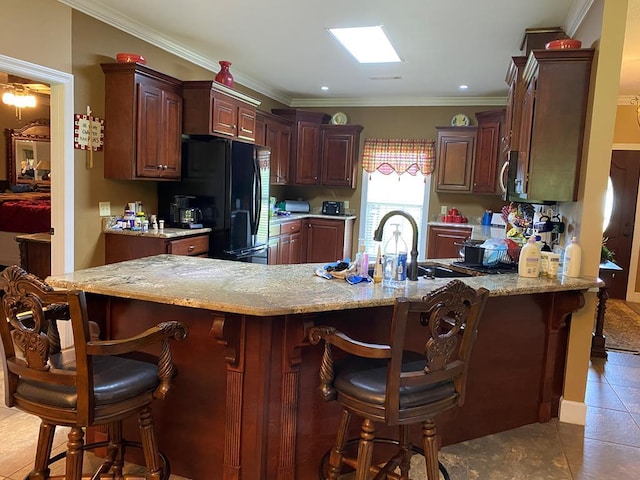 kitchen featuring crown molding, a skylight, kitchen peninsula, and black fridge