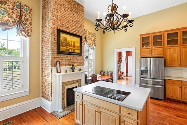 kitchen featuring black electric stovetop, light hardwood / wood-style flooring, stainless steel refrigerator with ice dispenser, backsplash, and a fireplace