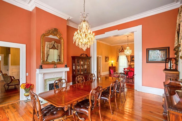 dining area featuring a notable chandelier, wood-type flooring, ornamental molding, and a high end fireplace