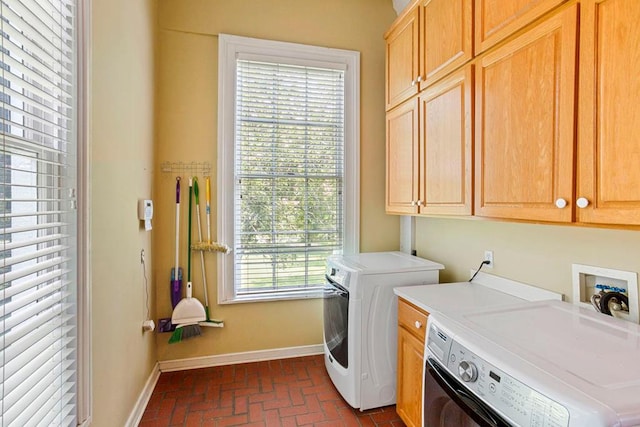 laundry area featuring washing machine and clothes dryer, plenty of natural light, and cabinets