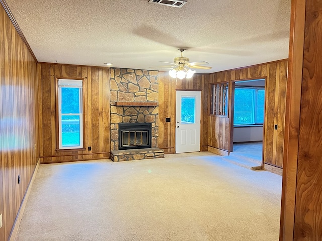 unfurnished living room with a stone fireplace, ceiling fan, plenty of natural light, and light colored carpet