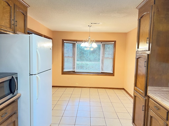 kitchen with an inviting chandelier, white refrigerator, a textured ceiling, decorative light fixtures, and light tile patterned flooring