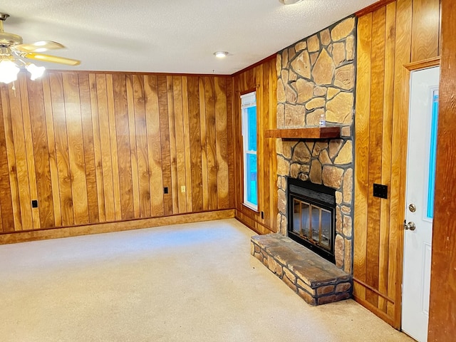 unfurnished living room featuring ceiling fan, wooden walls, a textured ceiling, light carpet, and a fireplace