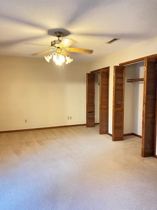 unfurnished bedroom featuring a textured ceiling, ceiling fan, light carpet, and two closets