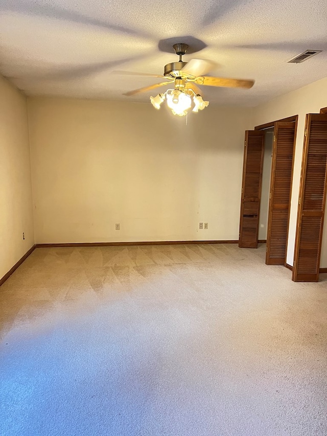 unfurnished bedroom featuring multiple closets, ceiling fan, light carpet, and a textured ceiling