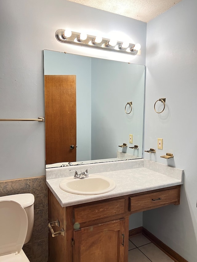 bathroom with vanity, tile patterned floors, toilet, a textured ceiling, and tile walls