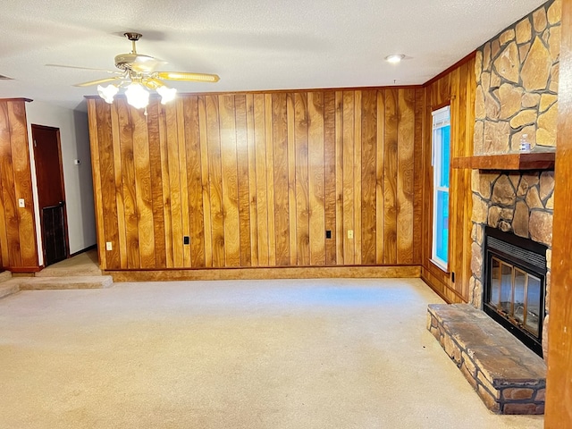 unfurnished living room featuring ceiling fan, light colored carpet, a fireplace, and wooden walls