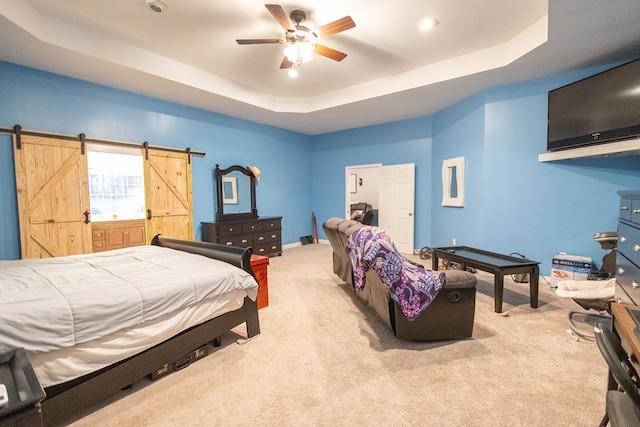 bedroom featuring ceiling fan, a barn door, a raised ceiling, and light colored carpet