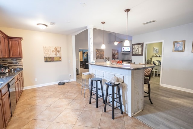 kitchen featuring tasteful backsplash, stainless steel dishwasher, dark stone countertops, pendant lighting, and a kitchen bar