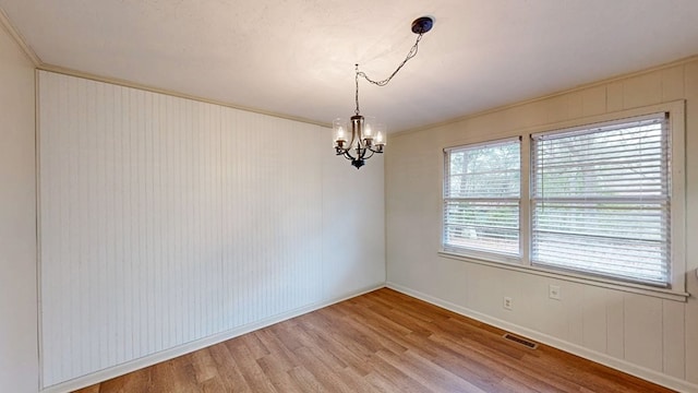 empty room with hardwood / wood-style flooring, ornamental molding, and an inviting chandelier