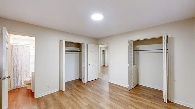 unfurnished bedroom with two closets, ensuite bathroom, and light wood-type flooring