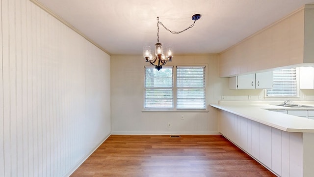 unfurnished dining area with crown molding, sink, an inviting chandelier, and light wood-type flooring