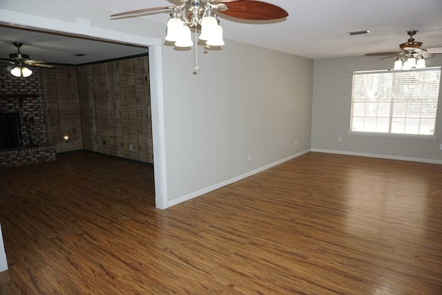 empty room with ceiling fan, dark hardwood / wood-style flooring, and a brick fireplace