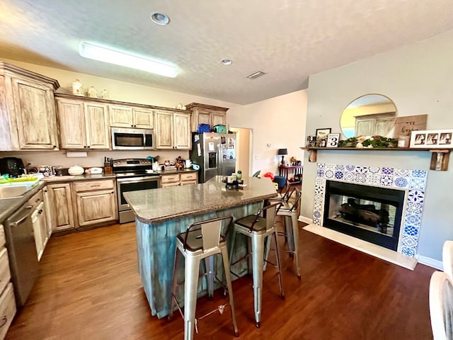 kitchen with a center island, a kitchen breakfast bar, light brown cabinetry, stainless steel appliances, and a tiled fireplace