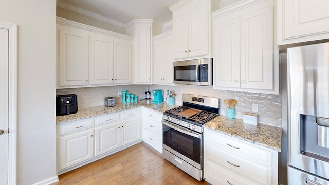 kitchen featuring white cabinetry, light wood-type flooring, appliances with stainless steel finishes, light stone countertops, and backsplash