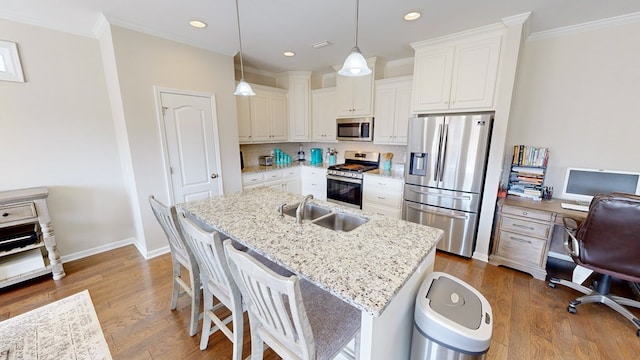 kitchen with sink, pendant lighting, stainless steel appliances, a kitchen island with sink, and white cabinets