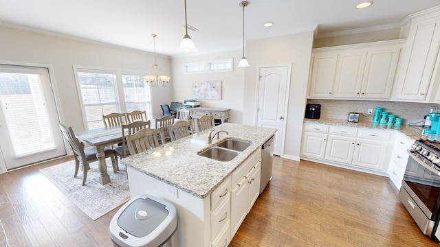 kitchen with sink, hanging light fixtures, stainless steel appliances, white cabinets, and a center island with sink