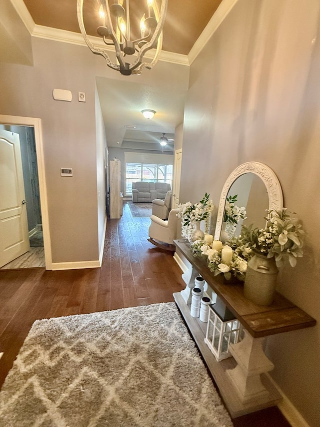 hallway with dark wood finished floors, a notable chandelier, crown molding, and baseboards