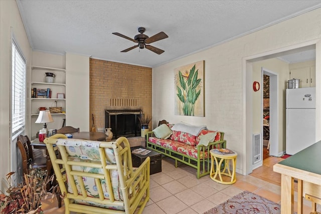 tiled living room featuring ceiling fan, a textured ceiling, brick wall, and a brick fireplace