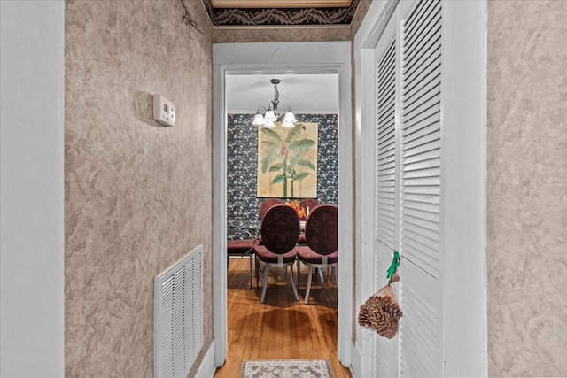 hallway featuring ornamental molding, wood-type flooring, and an inviting chandelier