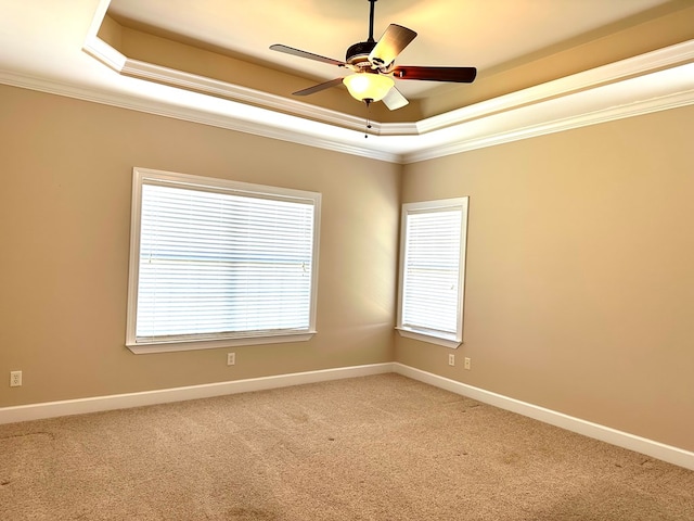 empty room with a tray ceiling, baseboards, light colored carpet, and ornamental molding