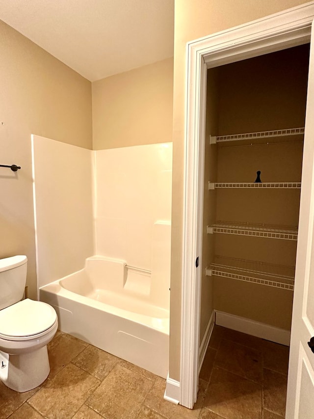 bathroom with a bathing tub, toilet, stone finish flooring, and baseboards