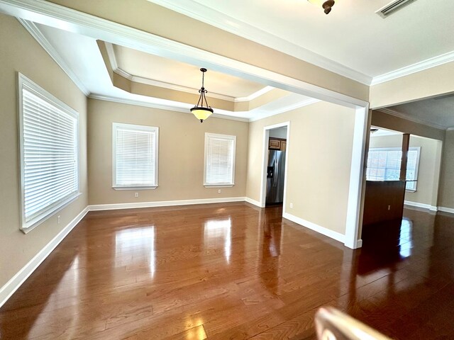 spare room featuring visible vents, a raised ceiling, wood finished floors, and ornamental molding