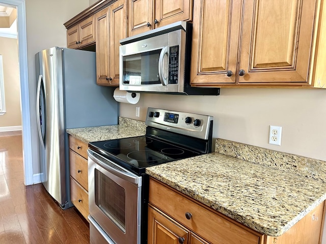 kitchen with brown cabinets, stainless steel appliances, dark wood-type flooring, and baseboards