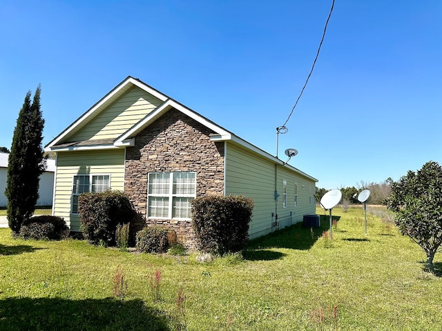 view of side of property featuring stone siding, a lawn, and central AC unit