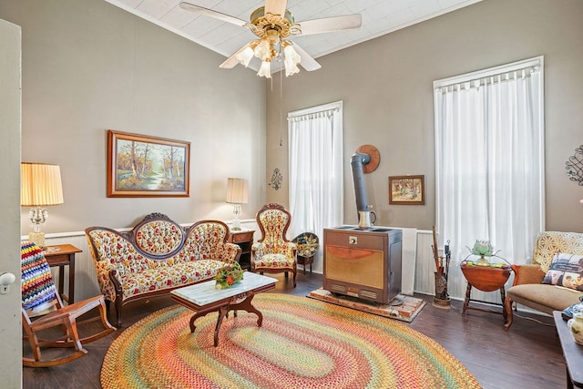 living area with plenty of natural light, wood finished floors, a wood stove, and a ceiling fan
