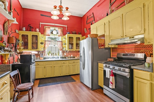 kitchen with light wood finished floors, stainless steel appliances, tasteful backsplash, under cabinet range hood, and a notable chandelier