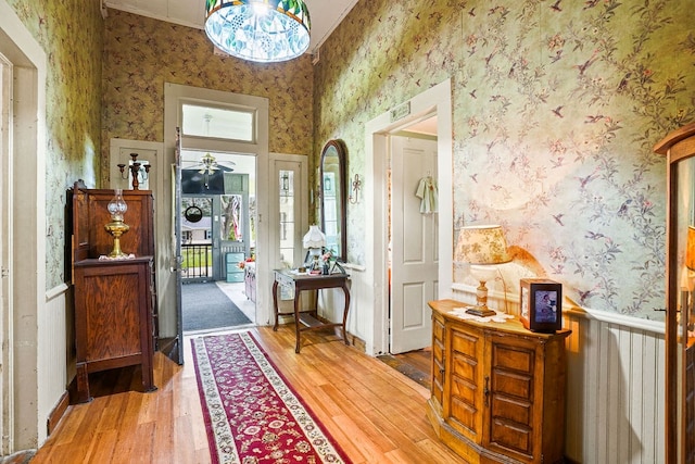 foyer entrance with wood-type flooring, wallpapered walls, and wainscoting
