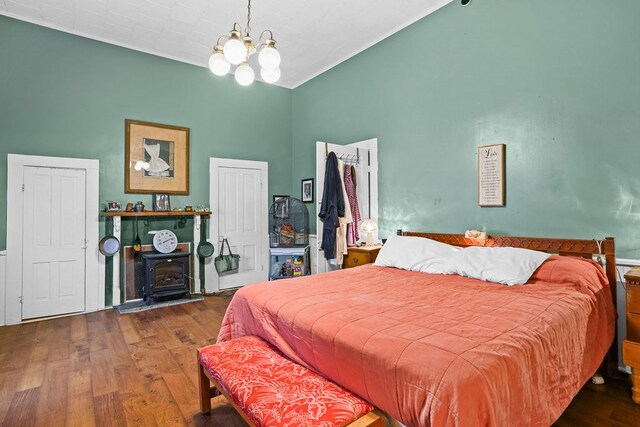 bedroom with an inviting chandelier, wood finished floors, vaulted ceiling, and a wood stove