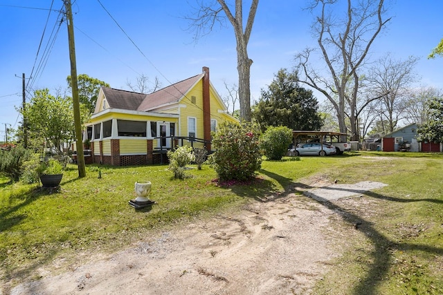 view of side of property featuring dirt driveway, a sunroom, a yard, and a chimney