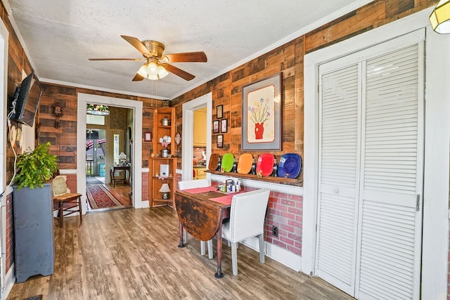 dining area featuring a textured ceiling, wooden walls, wood finished floors, and a ceiling fan