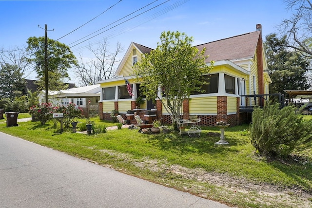 view of front of property featuring a chimney, brick siding, a sunroom, and a front lawn