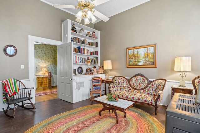 living area with ornamental molding, a high ceiling, a wainscoted wall, a ceiling fan, and wood finished floors
