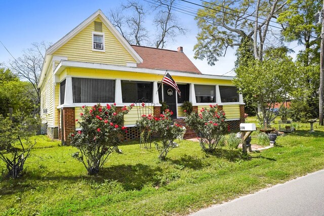 view of front of house with a sunroom, a chimney, brick siding, and a front yard