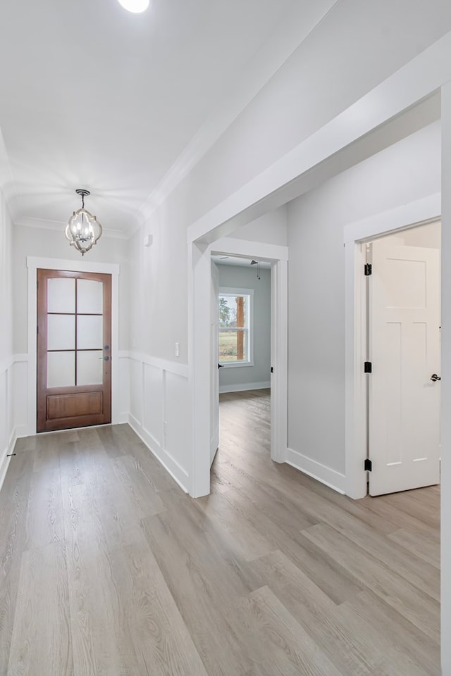 entryway with light hardwood / wood-style flooring, ornamental molding, and a chandelier